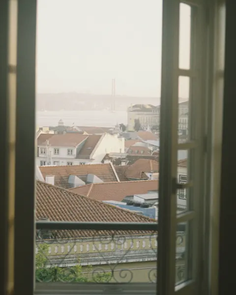 Janela aberta para os telhados de Lisboa, com o rio ao fundo.
