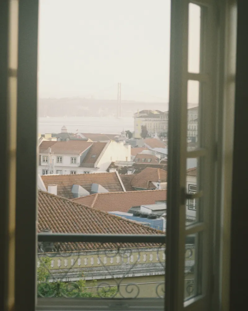 Janela aberta para os telhados de Lisboa, com o rio ao fundo.